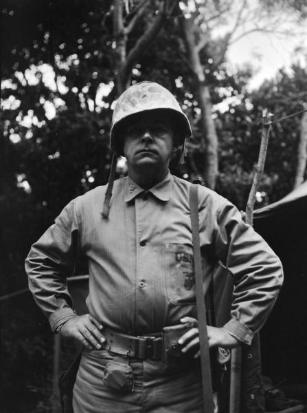 Captain Don Knowlton, a U.S. Marine division Surgeon, posing for a photograph outdoors in Okinawa, Japan. He is wearing fatigues and a helmet and is standing outside of a tent.