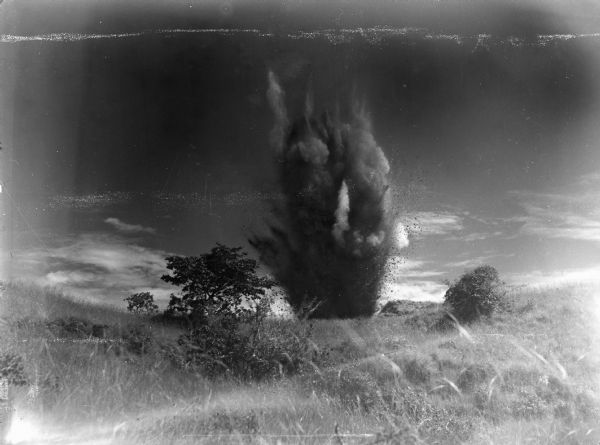 An explosion set by trainees at Rio Hato Infantry Artillery School in Panama in a rural area, with trees and shrubs in the forground.