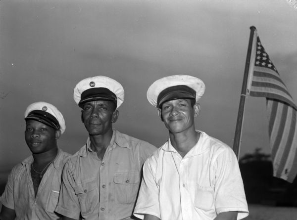 Colonel O'Donnel, a commanding officer for the 14th Infantry, posing with two other soldiers. The three men are outside and there is an American flag behind them. All of the men are wearing brimmed hats and are in uniform.