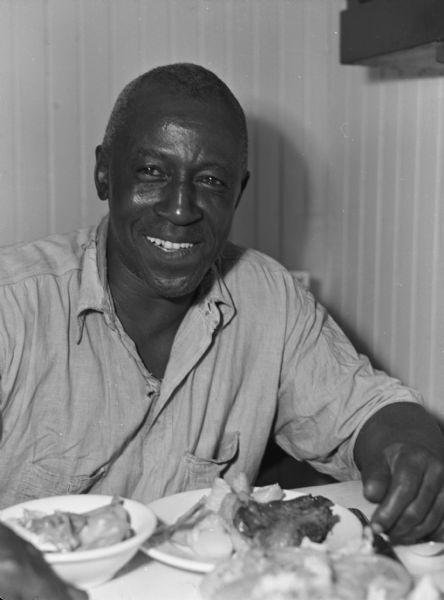A member of the United Fruit Company's S.S. <i>Santa Marta</i> eating dinner while in the Caribbean. The man is wearing a button-up shirt and is sitting at a table with food on a plate in front of him.