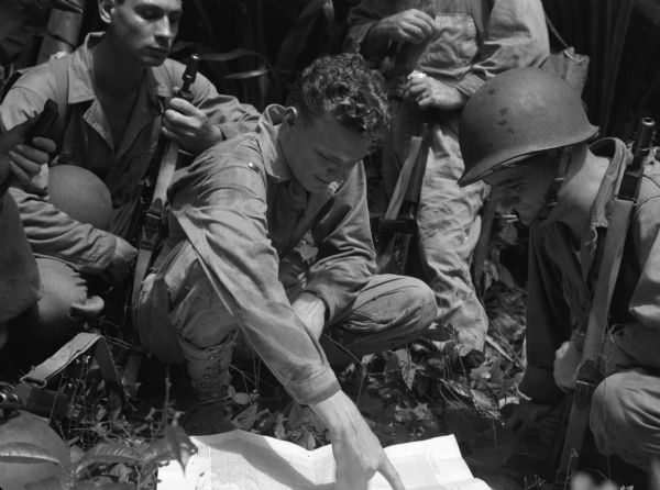 Officers and non-commissioned officers squatting to consult a map on the ground near Fort Davis, Panama. The men are wearing fatigues and have sub-machine guns.