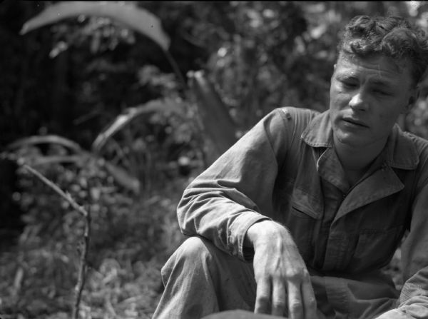 A soldier from the 18th Infantry near Fort Davis, Panama, rests after cutting through a jungle. He is wearing fatigues and is sitting down.