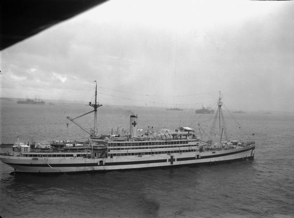 Elevated view of a newly commissioned hospital ship, the USS <I>Bountiful</I>, in the Ulithi Harbor. The ship was previously called the USS <I>Henderson</I> and was used as a troop transport ship. The ship is painted with the Red Cross insignia. Other ships are in the background.