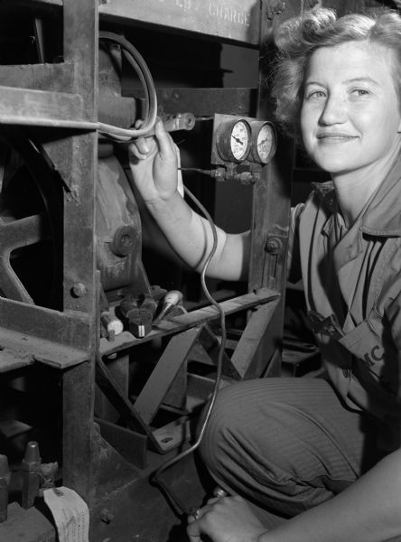 Private first class Ann D. Dozier, a refrigerating engineer from the United States Marine Corps Women's Reserve, posing for a photograph at the Mauna Loa Ridge encampment in Honolulu. She is wearing a jumpsuit and holding a tool to make an adjustment on a piece of machinery.