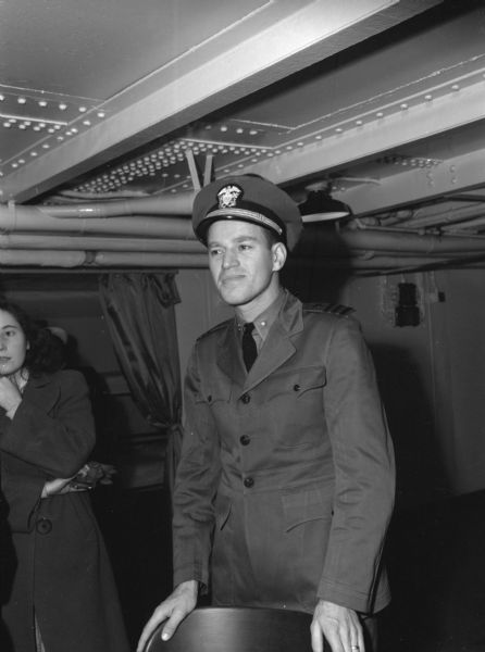 Lieutenant Commander J.C. Server, from the United States Navy Reserve, poses for a photograph aboard the USS <I>Relief</I> in the China Sea. He is wearing a uniform. Behind him is a woman in a long coat.