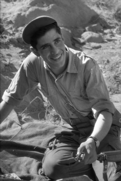 A young Algerian member of the National Liberation Front smiling and posing for a portrait with his gun.