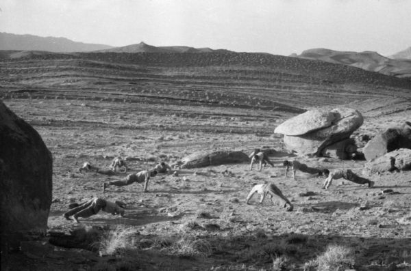 Algerian National Liberation Front members doing push-ups in the desert near boulders.