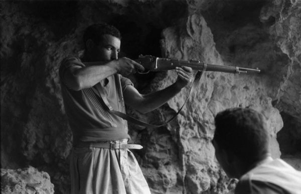 An Algerian member of the National Liberation Front aiming with his rifle from inside a cave.