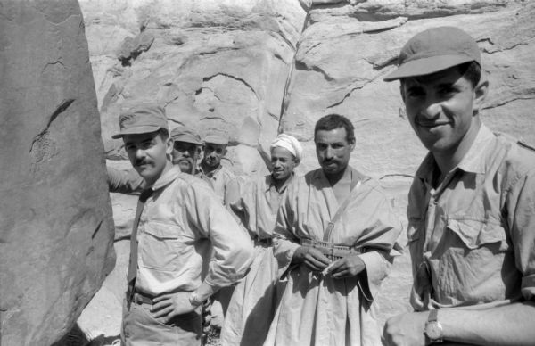 A group of National Liberation Front members posing for outside of a cave near large boulders.