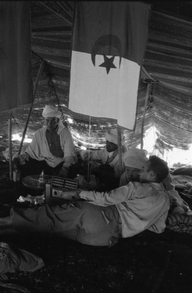 Algerian National Liberation Front members resting in a tent under the Algerian flag and listening to the radio.