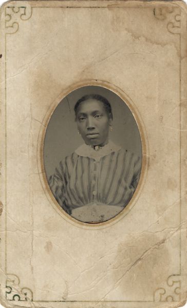 Tintype/ferrotype oval waist-up portrait of an African American woman in a striped shirtwaist with white collar and waistband, wearing earrings and a cameo brooch that appear to be hand-colored on the image.