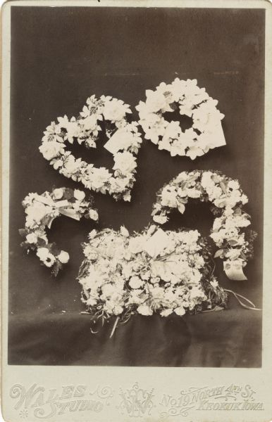 Funeral memorial card with one heart-shaped wreath and other floral wreaths decorated with ribbons and cards.