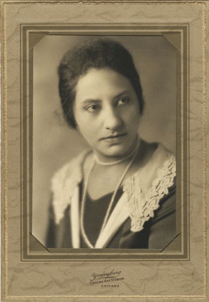 Quarter-length studio portrait of an African American woman wearing a long pearl double strand necklace and a dress trimmed with a lace-edged collar.