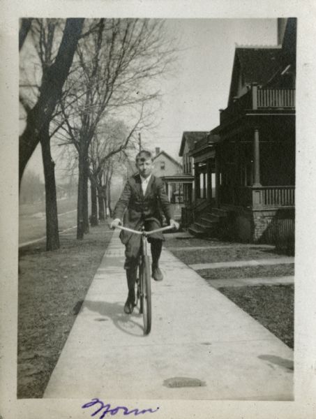 "Norm" riding a bicycle down a sidewalk on a residential street.    