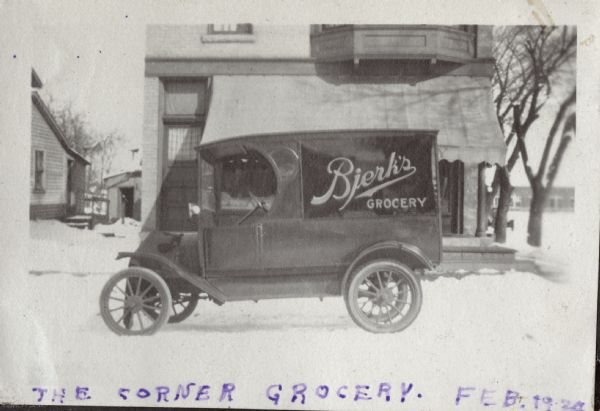 Side view of a Bjerk's Grocery wagon parked on a snowy street in front of the shop, which was located at 1 N. Blair Street (at E. Washington Avenue).
