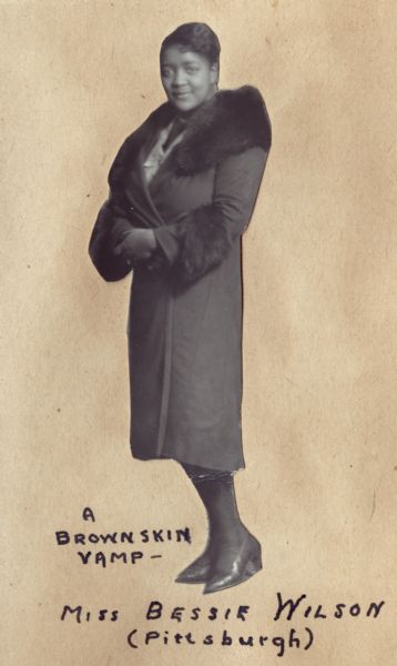 Full-length cut-out portrait of Bessie Wilson wearing a fur-trimmed overcoat.