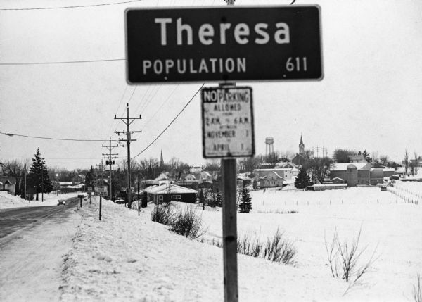 "In the early morning hours, a new month dawns on the small village of Theresa.  The village is now in the 130th year of its existence."  The village marker reads, "Theresa, Population 611."