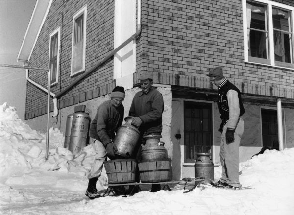 "A sled was used to convey the milk cans. Shown are Ralph Widmer, Bill Breitag, and Ken Reimer."