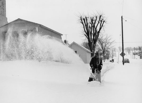 Winter scene of Ralph Widmer, the photographer's brother, using a snow blower.  Caption:  "Ralph Widmer blows snow off the sidewalk along Wisconsin Street."