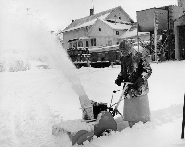 Winter scene of Ralph Widmer, the photographer's brother, using a snow blower to clear a walkway on Wisconsin Street, Theresa, Wisconsin.
Written on back, "Ralph Widmer blows snow off the sidewalk along Wisconsin Street."