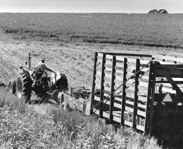 A man drives a tractor pulling a hay wagon through a field.