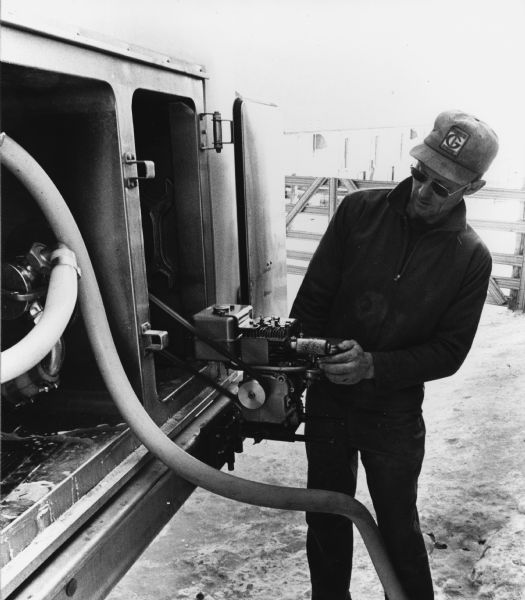 "For pumping out the milk at each farm, a small gas engine was used to power the truck's pump. Myron Weninger checks the pump on the Widmer Cheese bulk truck."