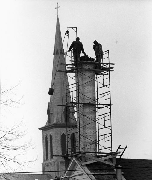"With the Catholic Church steeple looming in the background, Schuster Construction men work on the Widmer Cheese Factory chimney."