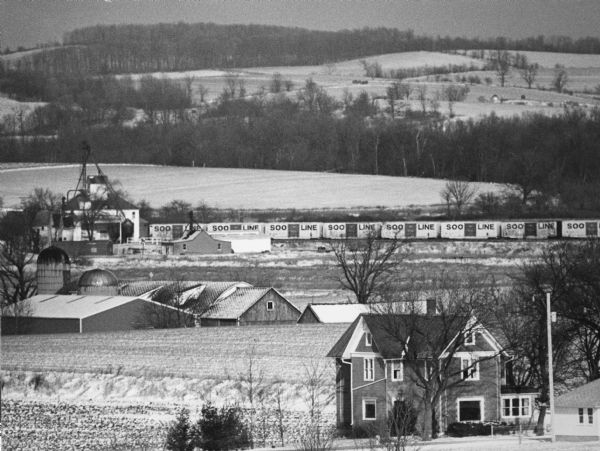 "This photo shows the John Steger home on the West Bend Road, foreground, the Willard Bogenschneider farm in the middle distance, and Theresa Station and the Soo Line cars beyond."