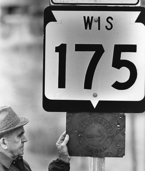 The 'Yellowstone Trail' at one time passed through the village. Les Beck displays a sign next to a present day road sign."