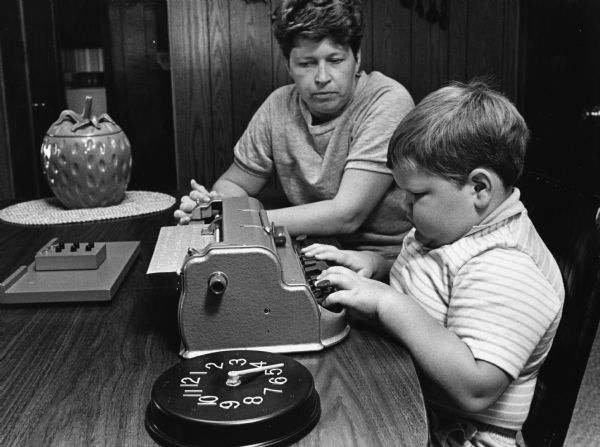 "Joel Bernhard, six years old, operates a six-key braille writer with the help of his mother Karen."