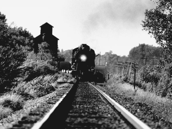 "The engineer waves as the steam locomotive bears down the track."