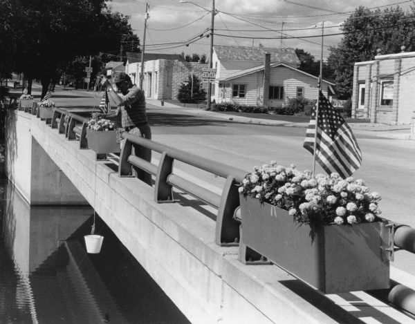 "Les Beck draws water from the Rock River to water eight colorful flower boxes put up by the Theresa Lions Club."