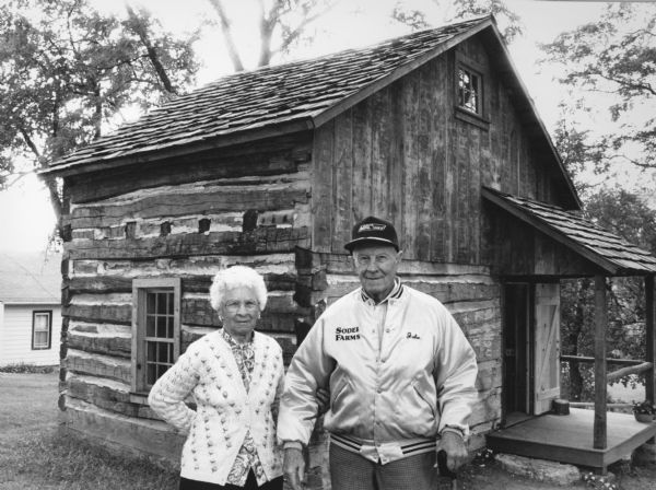 "John and Lydia Reklau pose by the Reklau Log House, the newest addition to the Theresa Historical Society grounds. The house was moved from a site two miles south of Theresa, where John, as a boy, visited his grandparents."