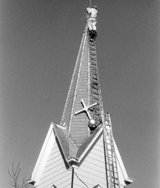 "High winds played havoc with the cross on St. Peter's Lutheran Church. Steeplejack, Tim McNitt, of Kiel was called in to rectify the 'leaning cross.'"