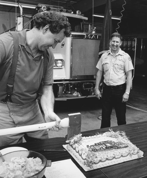 "Fire Chief Bob Bogenschneider 'cuts' a cake with a fire axe."