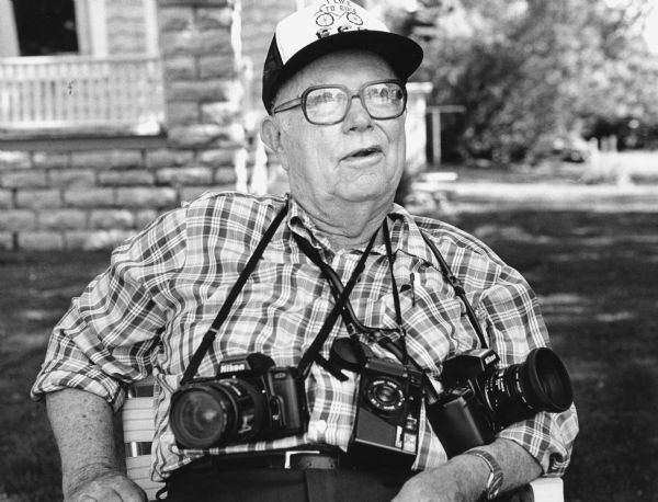 "Sporting three cameras, Mayville's famous photographer, Edgar G. Mueller, was photographed as he recorded the cupola restoration on the White Limestone School."