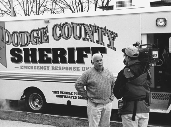 "A Channel 6 reporter-photographer interviews Dodge County Sheriff, Stephen Fitzgerald. Fitzgerald coordinated security around the crash scene."