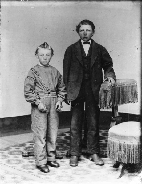 Copy from tintype by Alexander Krueger. Full-length portrait of Albert and Ernst Goetsch standing near a chair with decorative fringe.