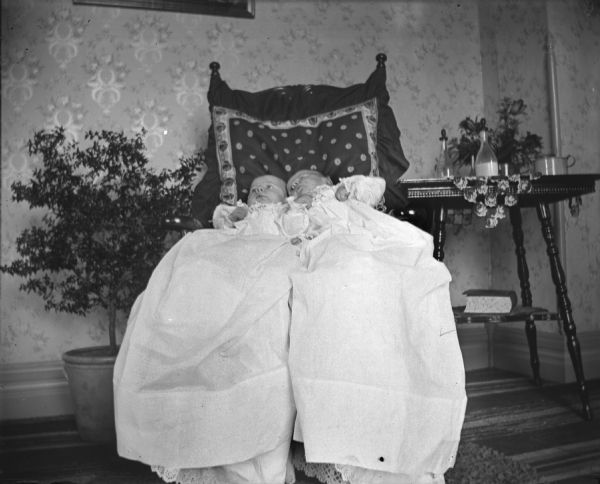 Edgar and Jennie Krueger lying together in a chair wearing long gowns. Bottles of milk are sitting on a side table. Portrait taken by Alexander Krueger.