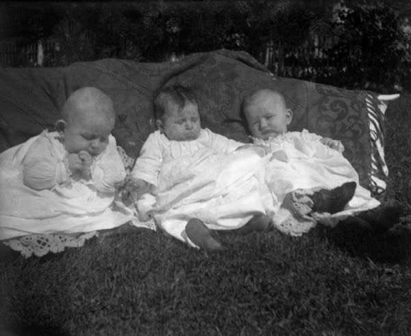 An outdoor portrait of Edgar and Jennie Krueger with Flora Gericke. The three infants are lying on the grass resting against a pillow covered with a cloth.