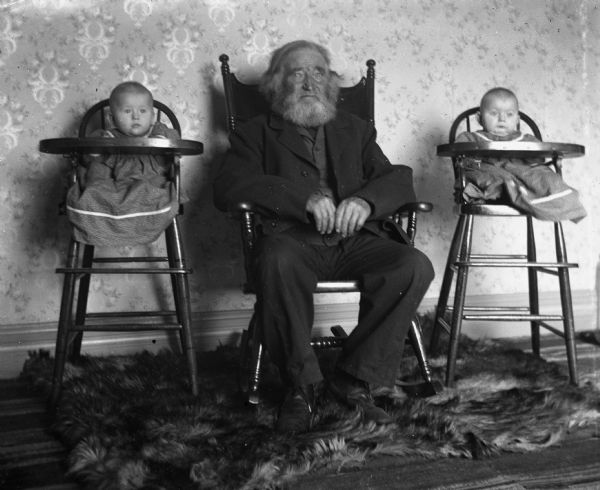William Krueger sits between the twins, Edgar and Jennie Krueger. There is a fur rug on the floor.