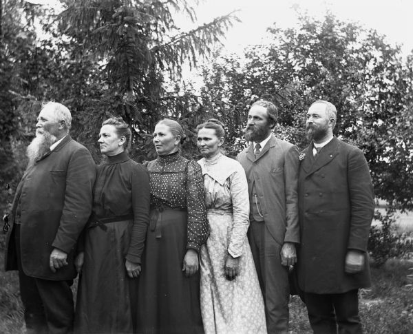 Portrait of members of the Krueger family, standing in a row, at an angle, looking to the left. From left to right are: August, Amelia, Bertha, Minnie, Albert, and Henry Krueger.
