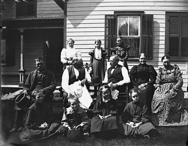 Group portrait of the Hable and Krueger families posing in the yard in front of a house. Two of the men are holding newspapers. Featured are Julius Hable, Mr. and Mrs. August Krueger, Sarah Krueger, and Hattie Braemer.