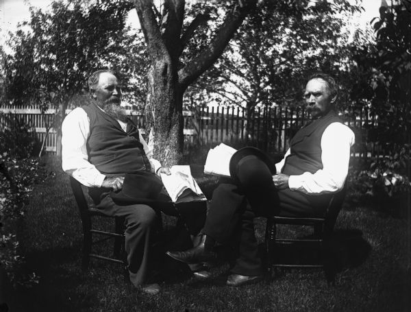 Outdoor portrait of August Krueger, left, and August Hable, right. The men, who met while Krueger worked on the great lakes, are holding hats and newspapers in Hable's yard.