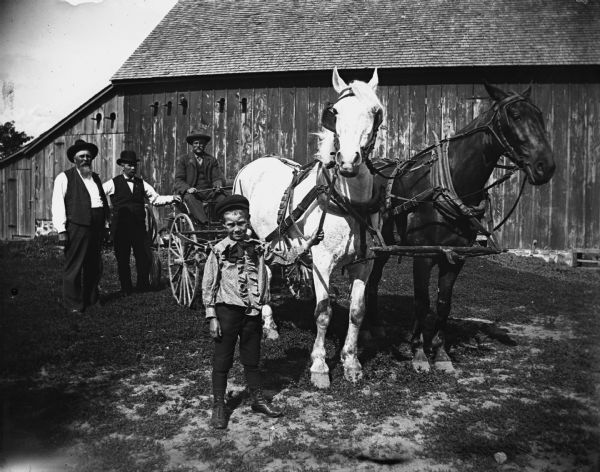 Julius Hable sitting in a horse-drawn buggy. Immediately to the left standing is August Hable, and August Krueger who is standing next to him. In the foreground, Clarance Hable is holding onto the horse's reins.