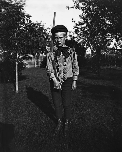 Clarance Hable standing in his yard holding a rifle and wearing a ruffled shirt.