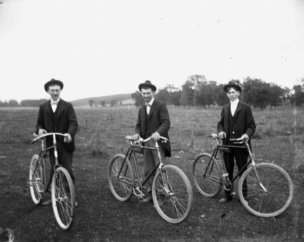 Three men are standing in a field holding their bicycles. From left to right are: Herman Reich, August Kressin, and Eddie Wendorf.