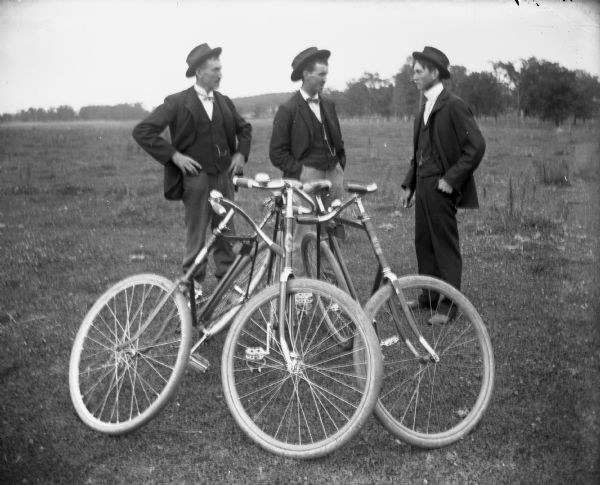 Three men are standing in a field, next to their bicycles. From left to right are: Herman Reich, August Kressin, and Eddie Wendorf.