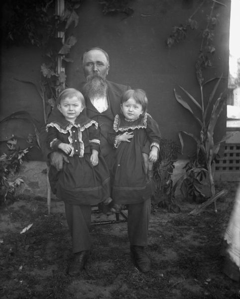 August Krueger, sitting, holding his two twin grandchildren on his lap.  Edgar and Jennie Krueger are aged one year, five months, twenty-one days.