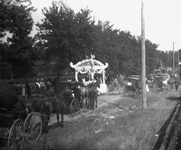 View of wagons and carriages lined up on a road on Concordia Island for a picnic.
